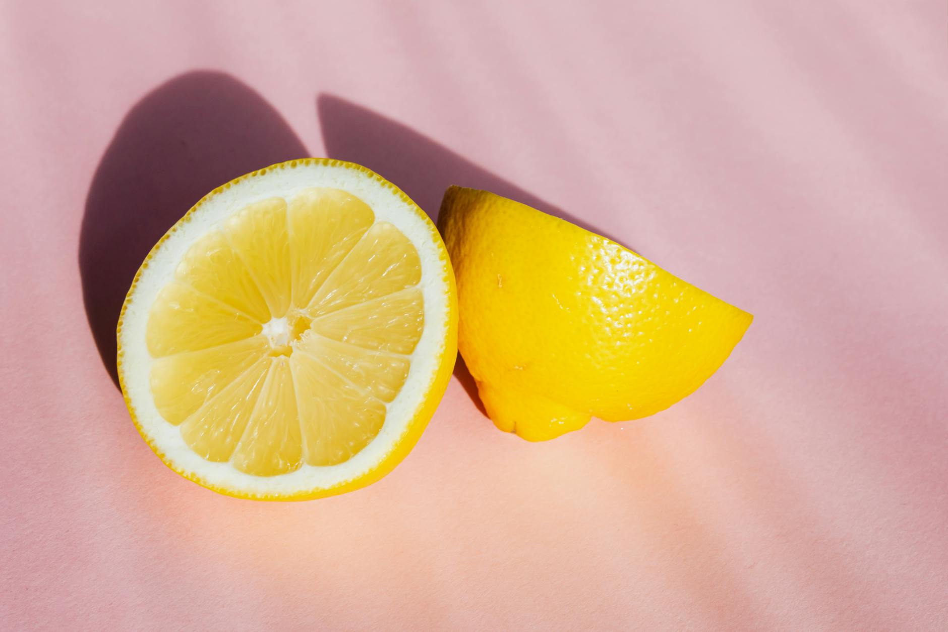 Fresh lemon halves on a soft pink background in bright natural light