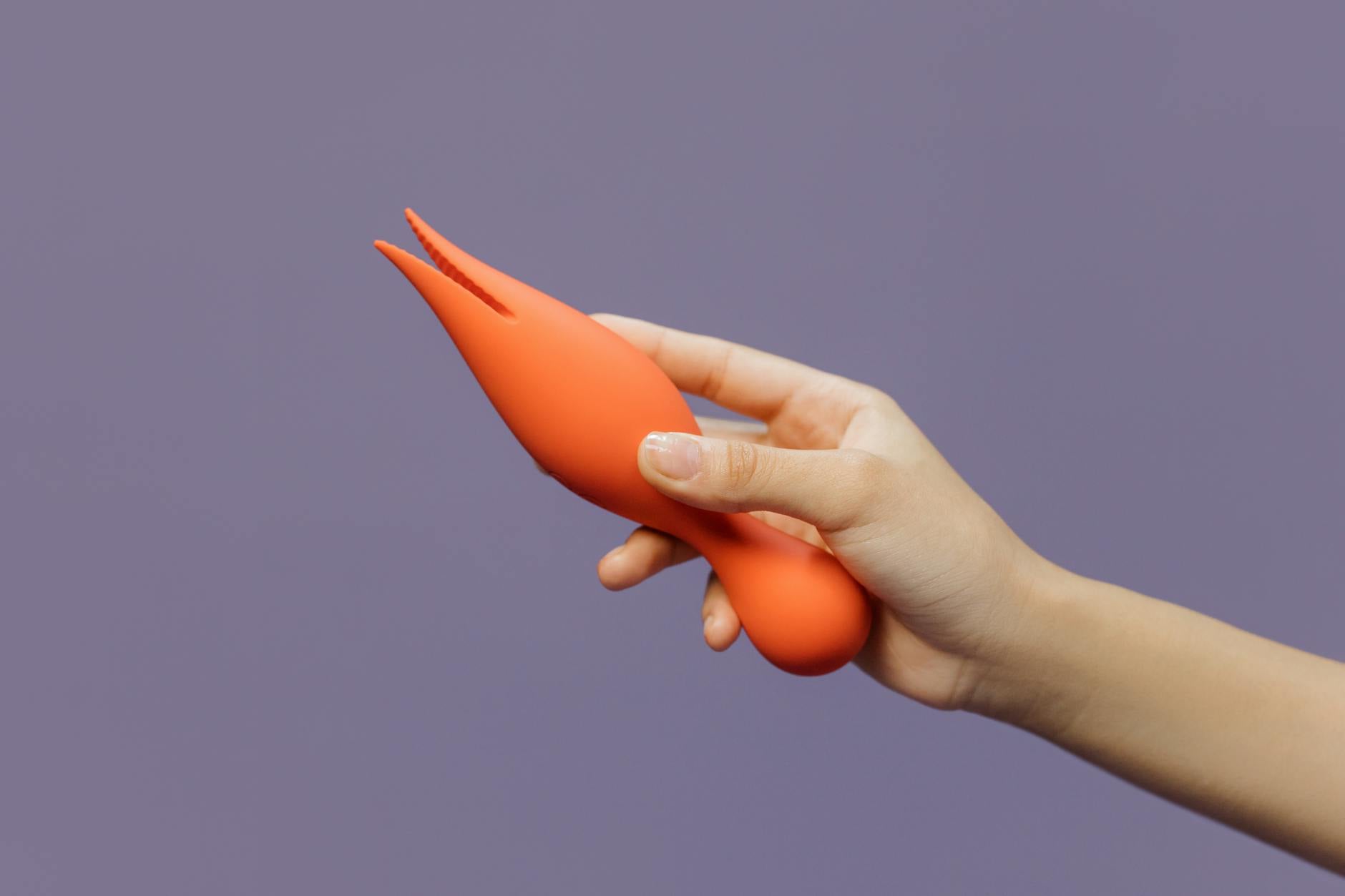 Close-up of a hand holding a lemon vibrator against a minimalistic purple backdrop, showcasing modern sensuality and shared intimacy.