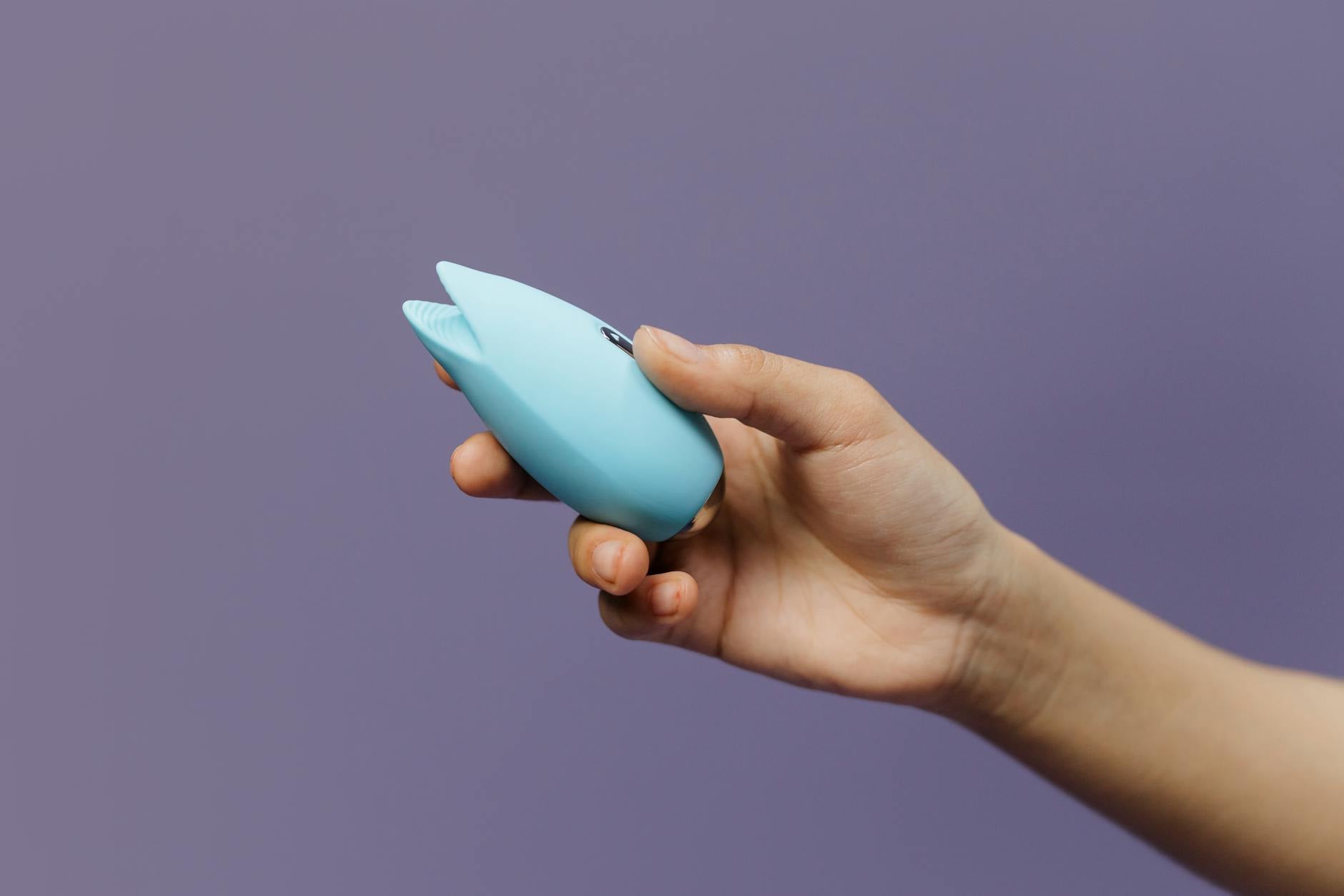 Hand holding a silicone clitoral vibrator against a purple background